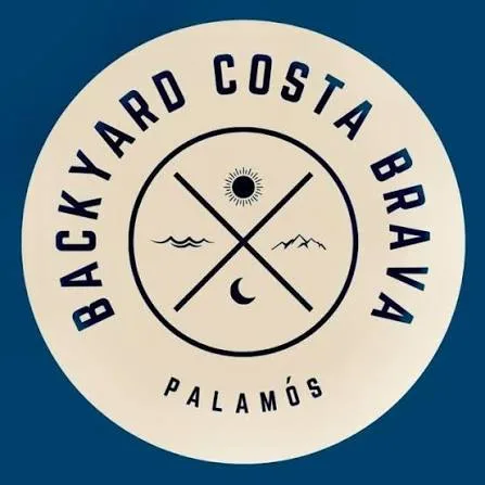 Cartel oficial del Backyard Costa Brava Palamós 2026: un organizador con micrófono saluda a una corredora en la zona de meta, junto a una carpa azul y público tras las vallas, con el texto "Obrim inscripcions 1 de juny de 2026" y el emblema circular "Backyard Costa Brava Palamós".